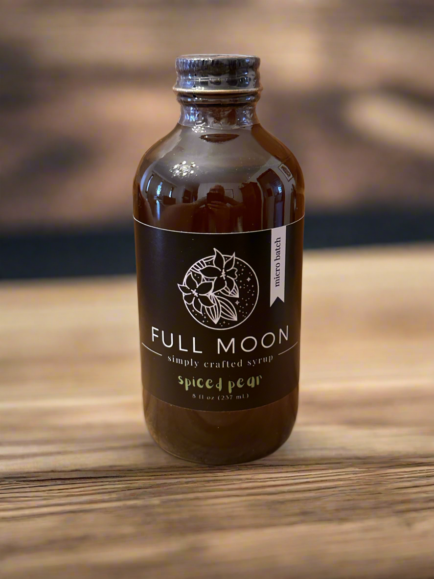 an amber bottle of pear simple syrup sits on a wooden surface