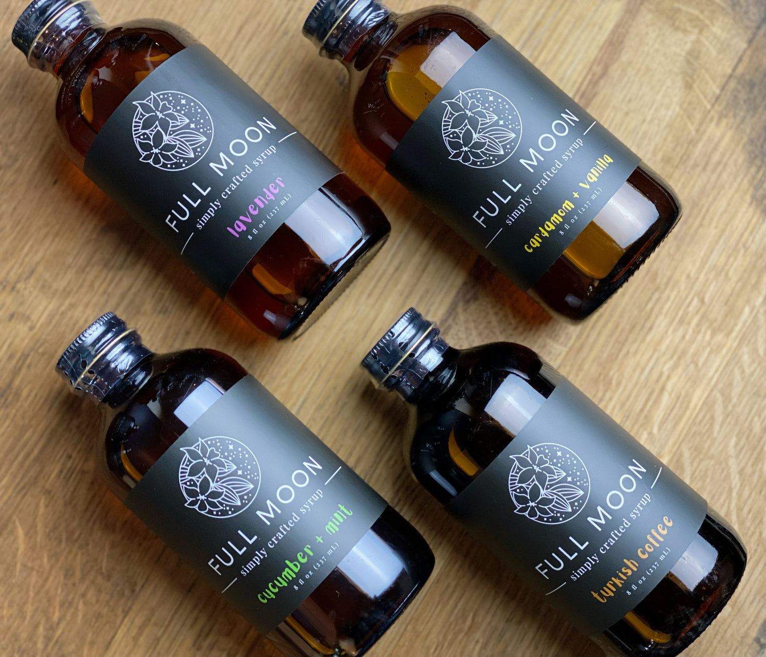 four amber glass bottles of simple syrups arranged on an oak table