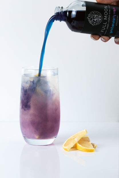 butterfly pea flower simple syrup is poured into a glass of lemonade, creating a color changing drink