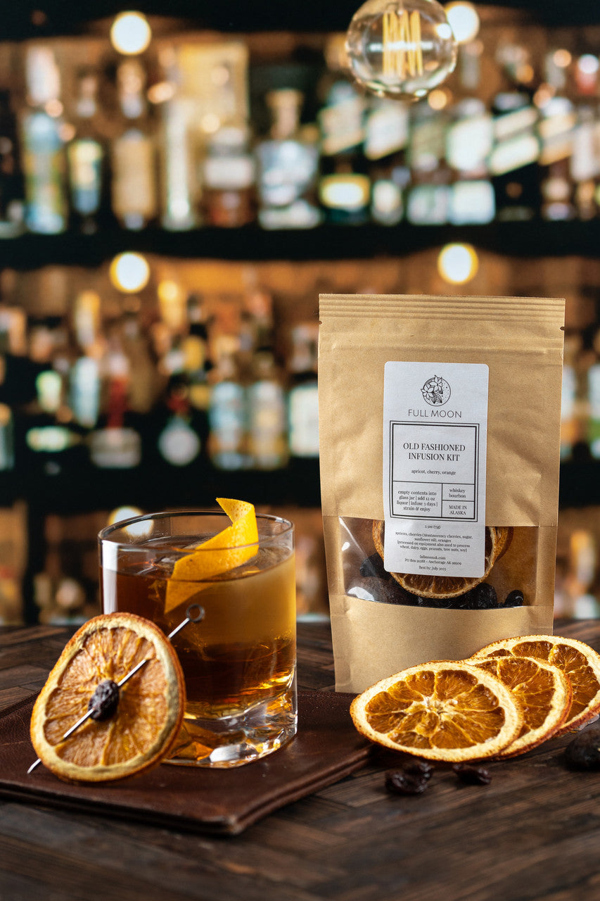 old fashioned cocktail kit sits next to an old fashioned cocktail on a wooden bar counter